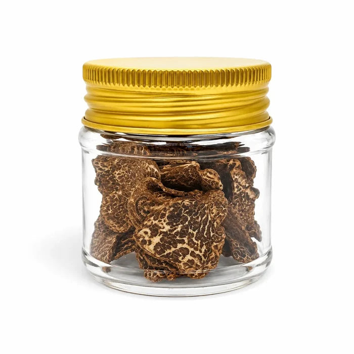 Dried Tuber borchii spring truffle slices in a clear glass jar with a gold lid