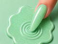 Green glittery slime with a hand dipping a finger into it on a green background